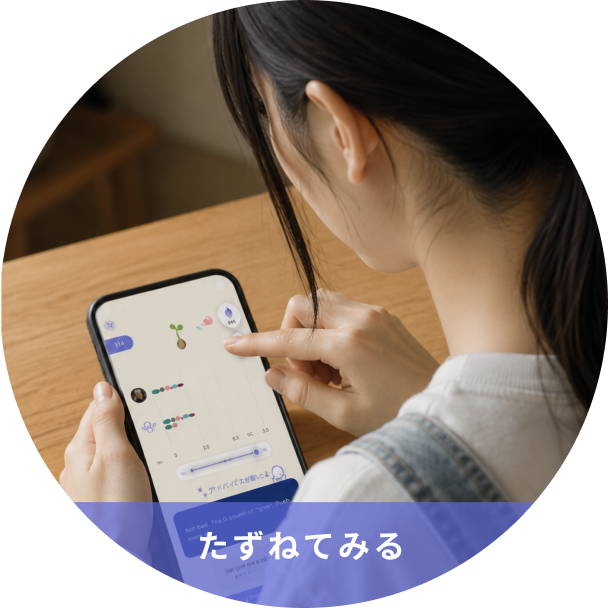 Person looking at a smartphone displaying a chart/graphs; a purple overlay with Japanese text 'たずねてみる' is visible at the bottom edge.