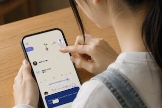 Person using a smartphone at a wooden table, tapping to view a chat conversation with blue message bubbles.